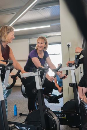 A group of women exercising on stationary bikes in a gym, focused on their workout. 